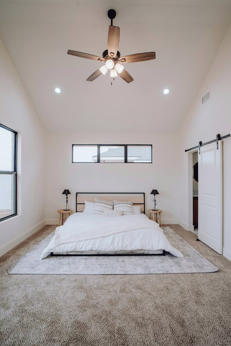 Electrician wiring a new ceiling fan with light fixture in a residential bedroom