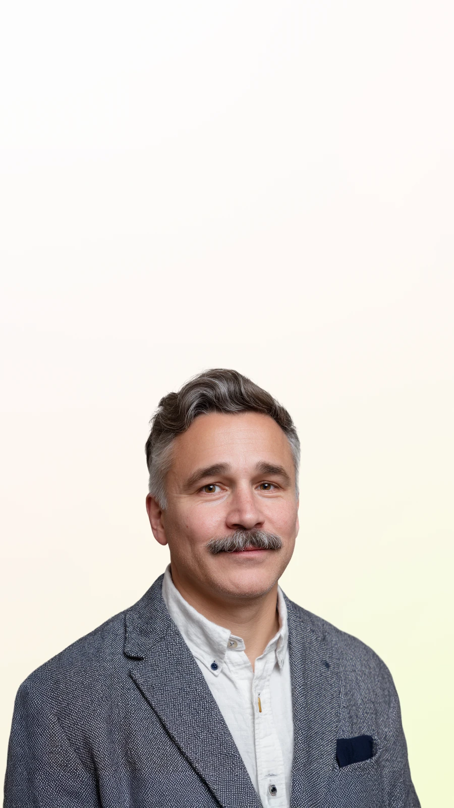 Middle-aged man with gray hair and mustache wearing a gray blazer and white shirt, smiling slightly.
