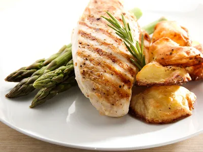 Grilled chicken breast served with roasted potato slices and steamed asparagus garnished with a sprig of rosemary.