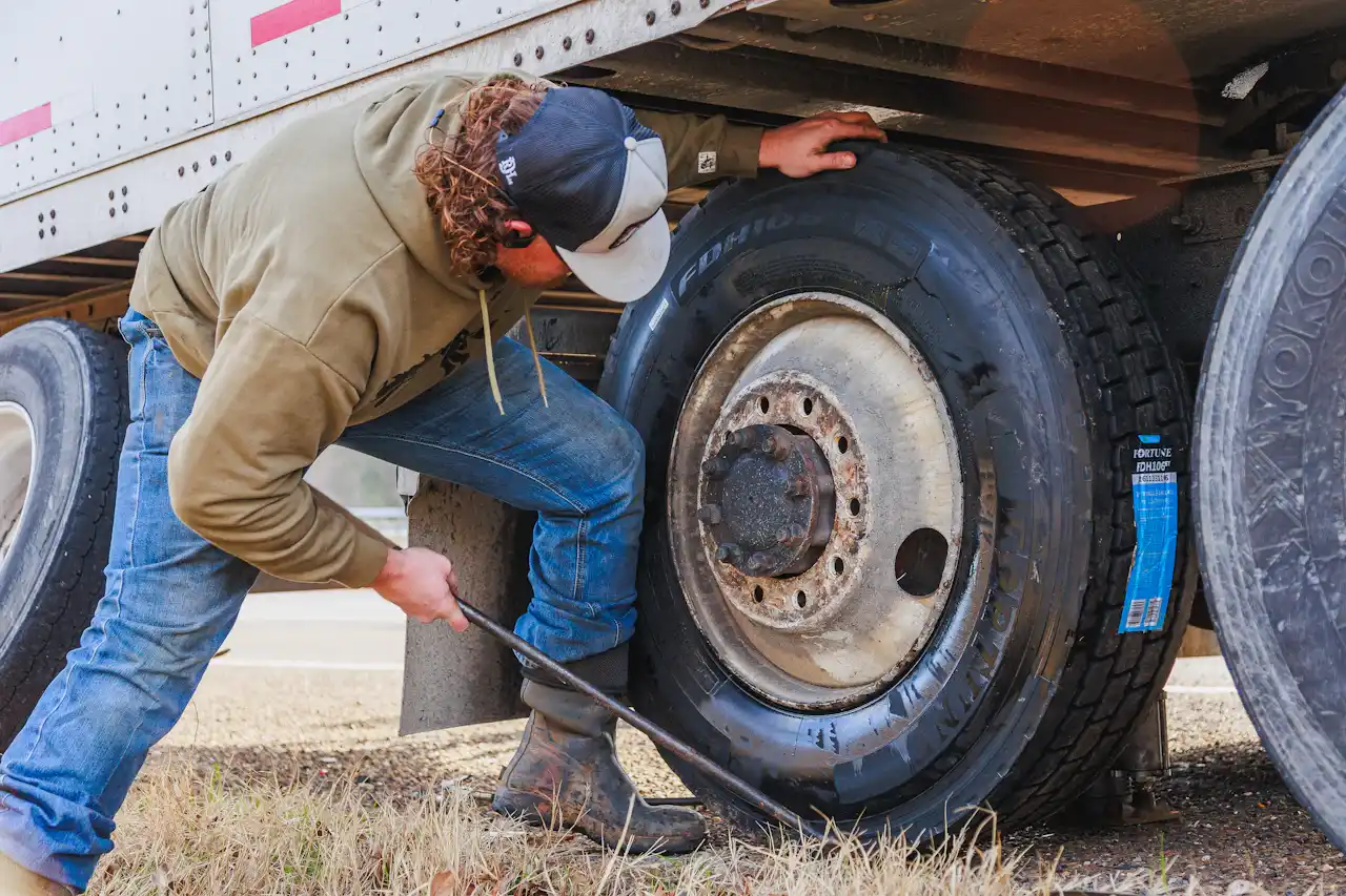 Tire service on a semi-trailer as a technician removes lug nuts with a breaker bar. The tire features Yokohama branding.
