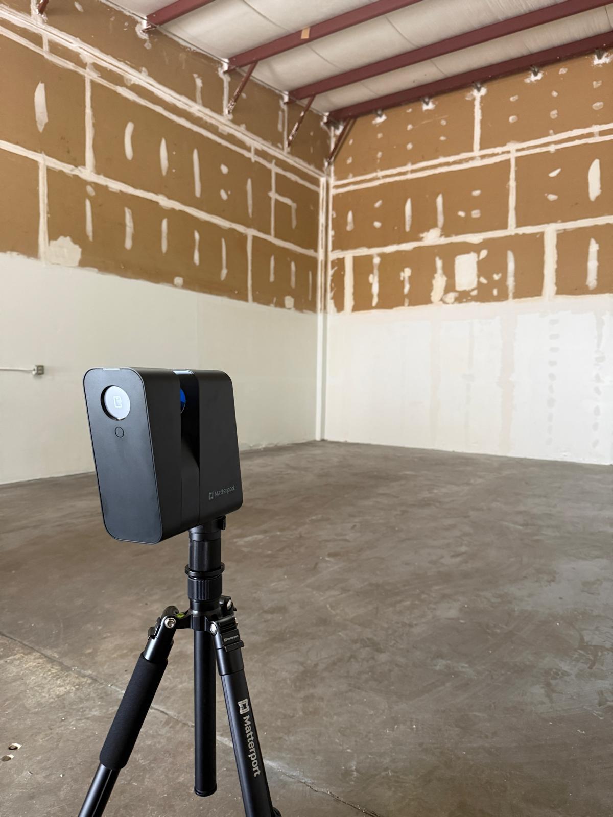 Matterport 3D camera mounted on a tripod inside an unfinished room with partially patched walls and concrete floor.