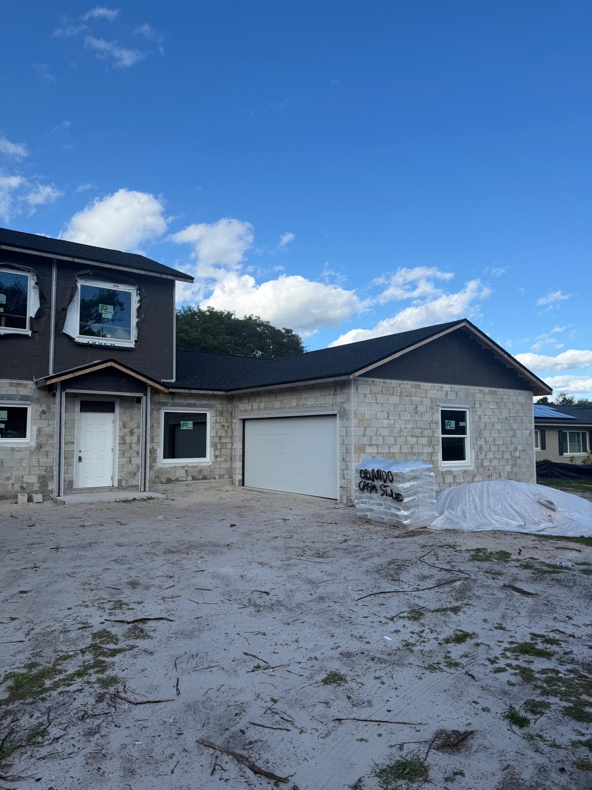Partially constructed two-story house with cinder block walls, a white garage door, and construction materials in front under a blue sky.