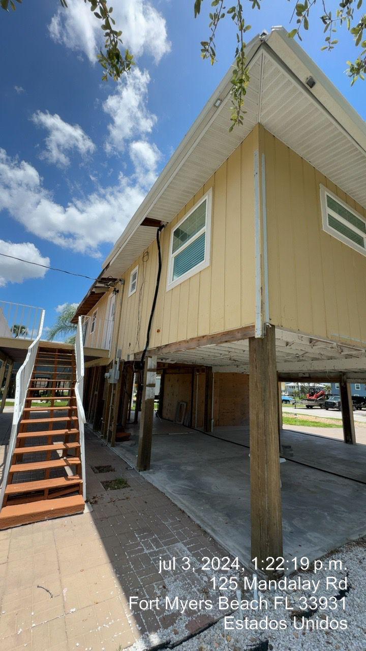 Elevated beige house with white trim, accessed by an exterior staircase under a partly cloudy blue sky.