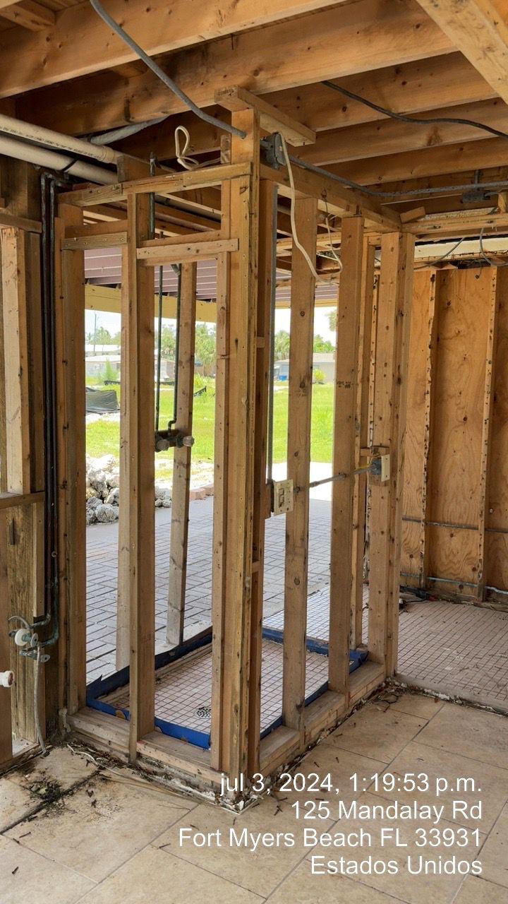 Wooden framing and exposed wiring inside a partially constructed building with tiled floor and outdoor view.