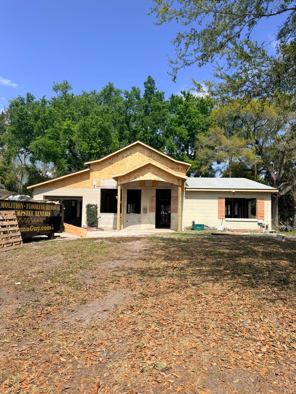 Single-story house under construction with plywood gable roof and large bare front yard covered with dry leaves.