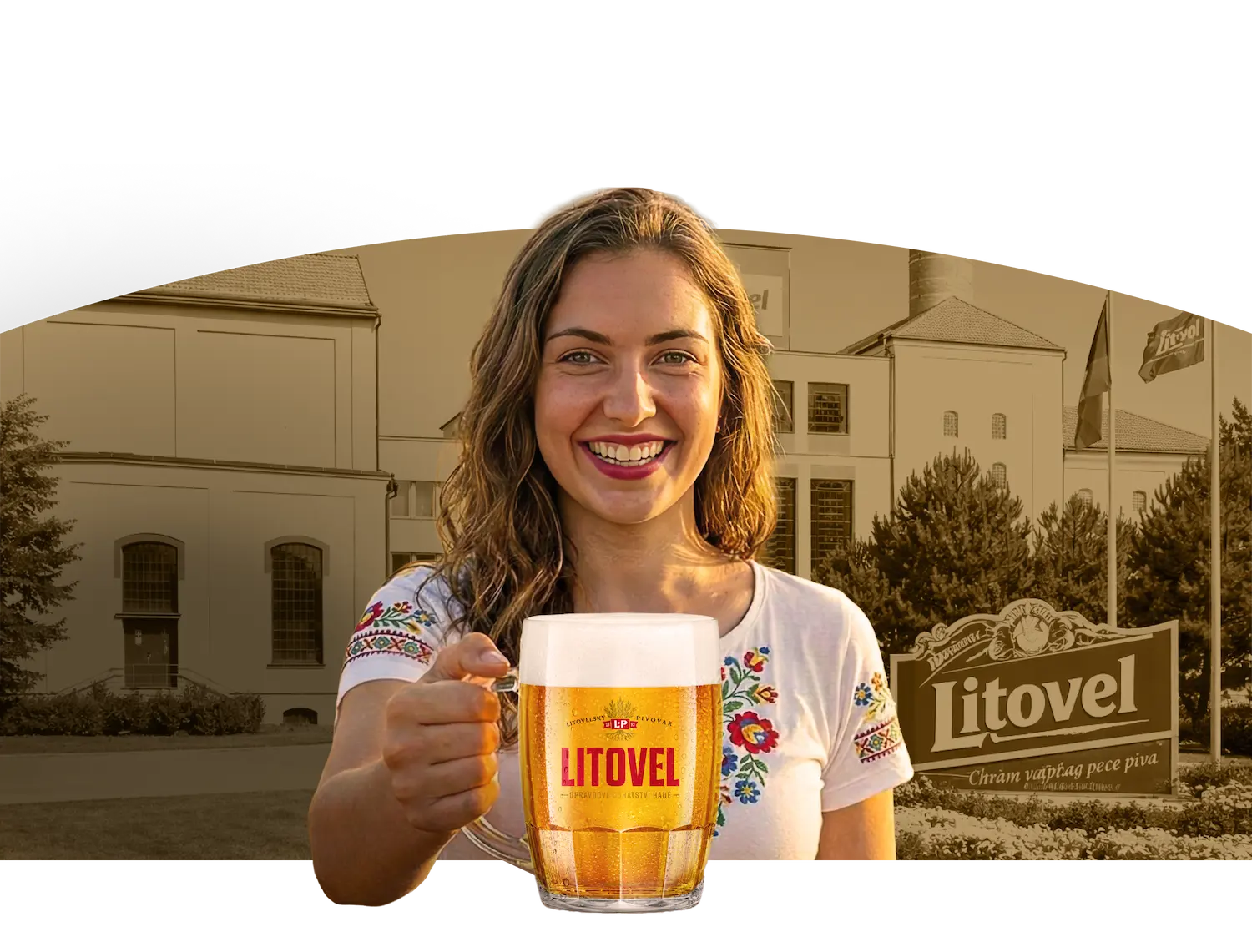Žena v tradičním vyšívaném tričku drží sklenici piva Litovel s pěnou před pivovarem Litovel.