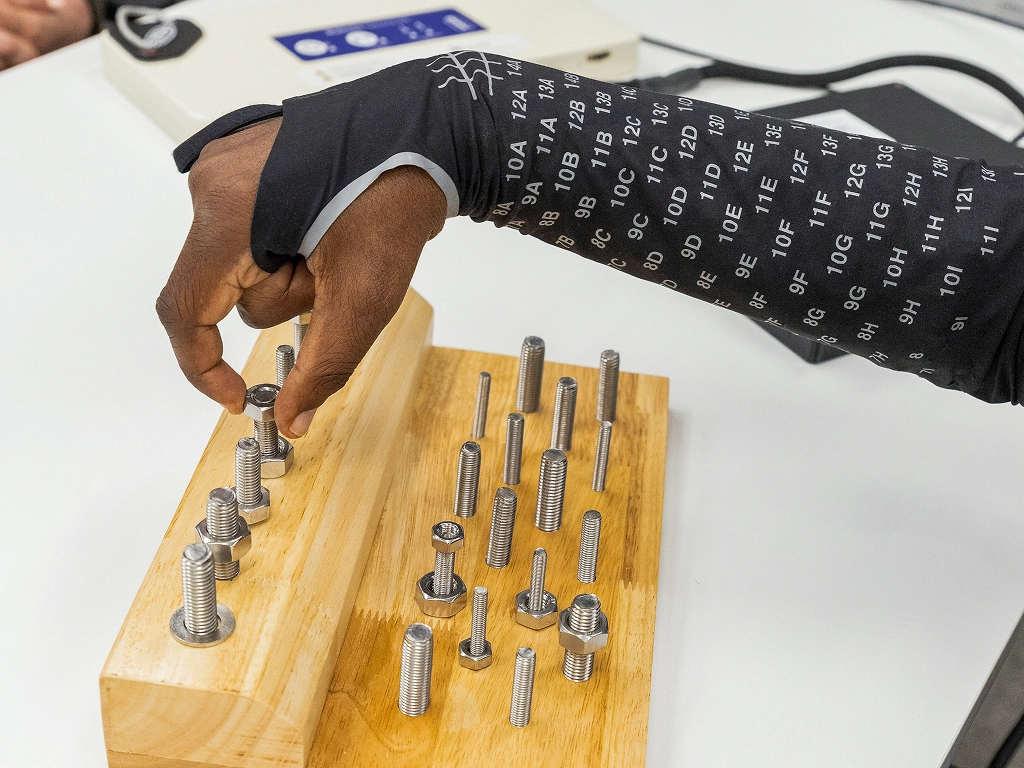 A mans arm with a black sleeve with numbers, arranging bolts and nuts on a wooden board.