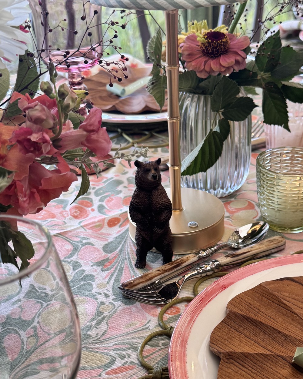 A small bear figurine among the flowers, glassware and place settings on the table.
