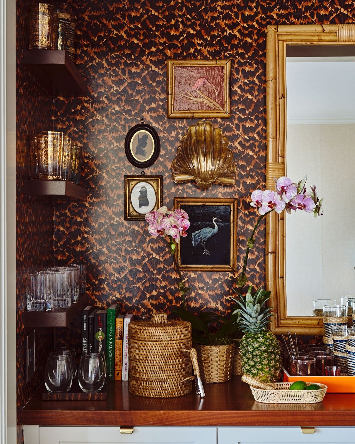 A small bar lined in tortoise wallpaper, with orchids, a pineapple and a bamboo mirror.