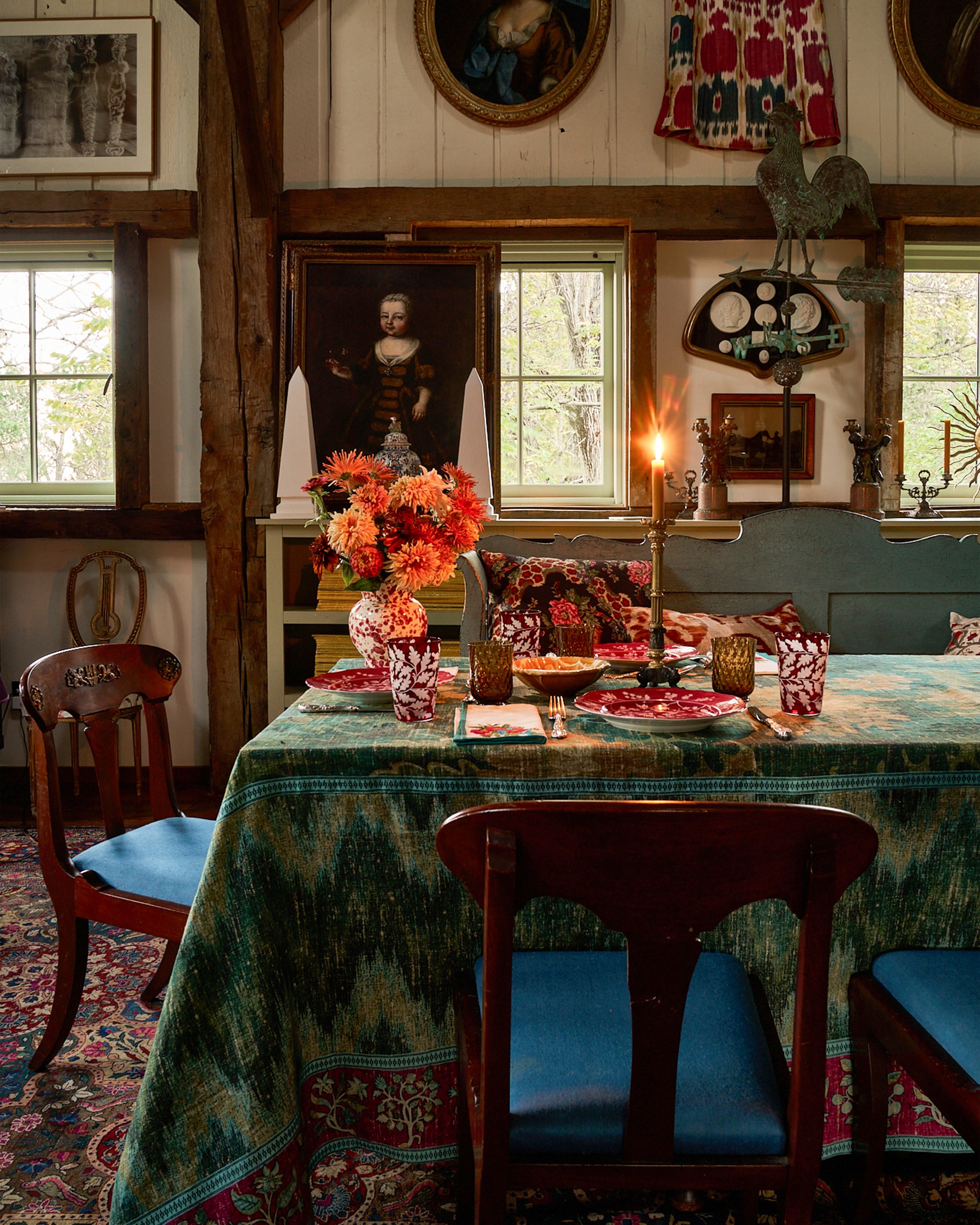 A candlelit dining table dressed in a green ikat tablecloth with red glassware, transferware and autumn flowers.