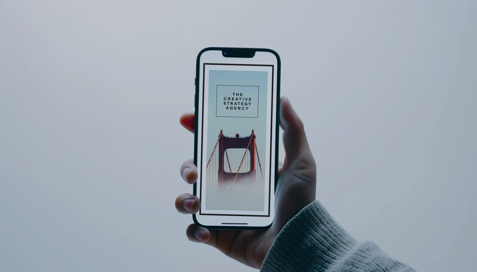 Hand holding smartphone showing an image of a red bridge with text The Creative Strategy Agency.