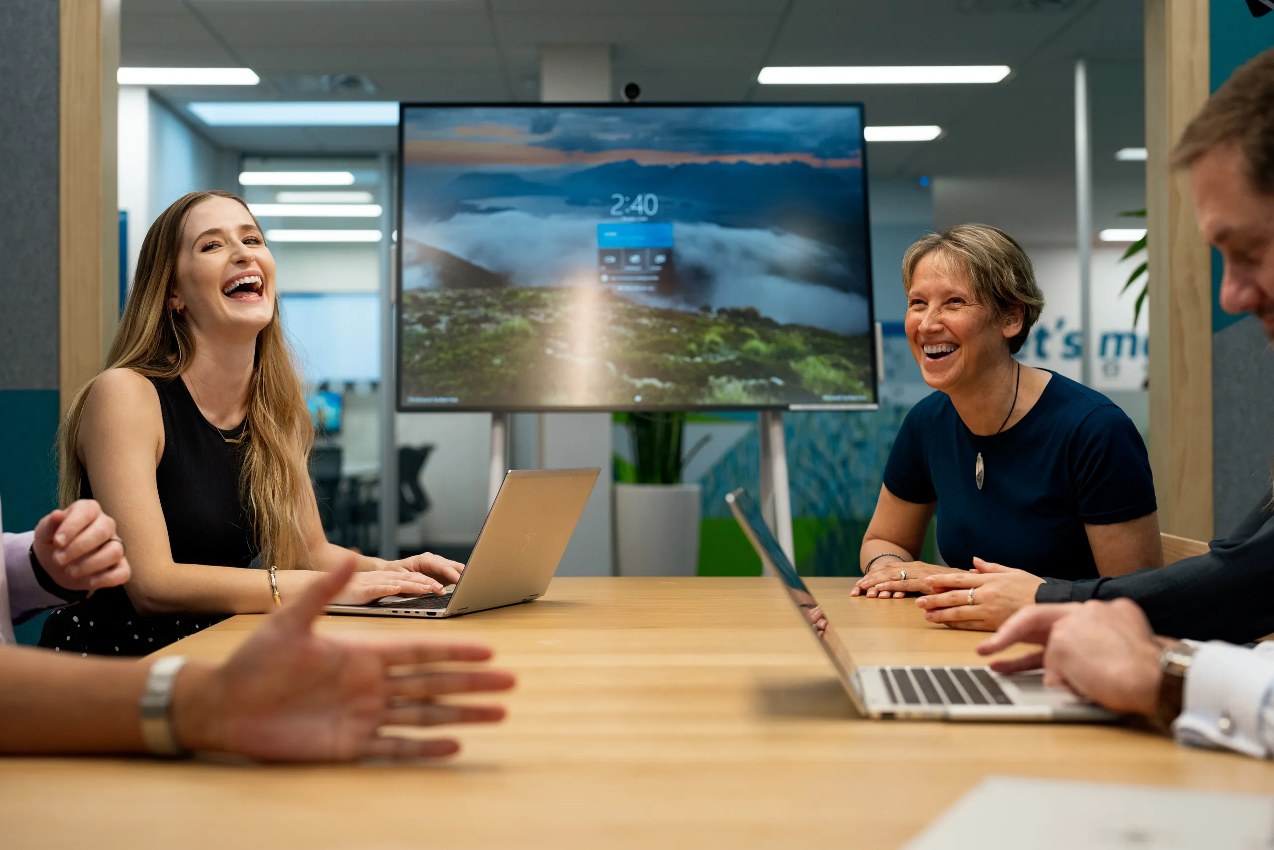 Three colleagues laughing and collaborating around a meeting table.