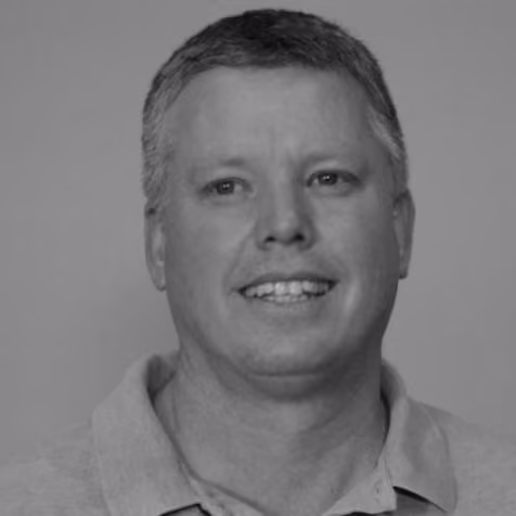 Headshot of a middle-aged man smiling with short hair wearing a collared shirt, against a plain background.