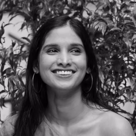 Black and white portrait of a smiling woman with long hair and hoop earrings against leafy background.