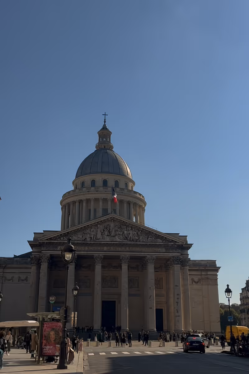 Le Panthéon à Paris vu par une journée ensoleillée avec des piétons et quelques voitures.