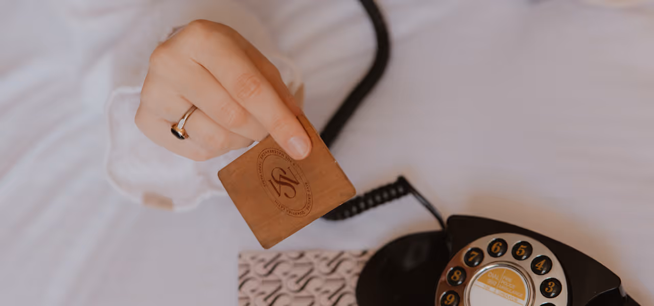 Une main tenant une carte en cuir au-dessus d'un téléphone à cadran noir vintage.
