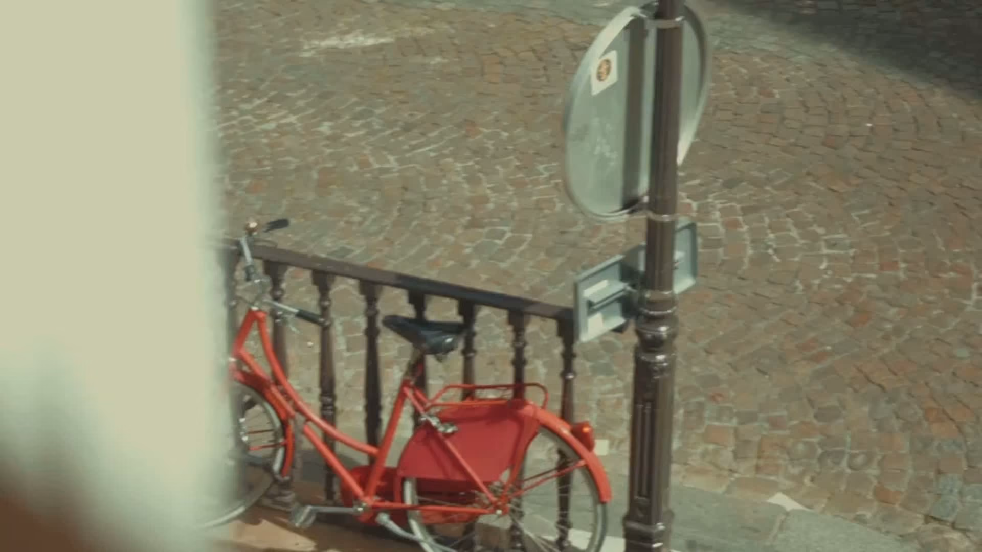 Vélo rouge garé à côté d'une barrière en métal sur un trottoir pavé.