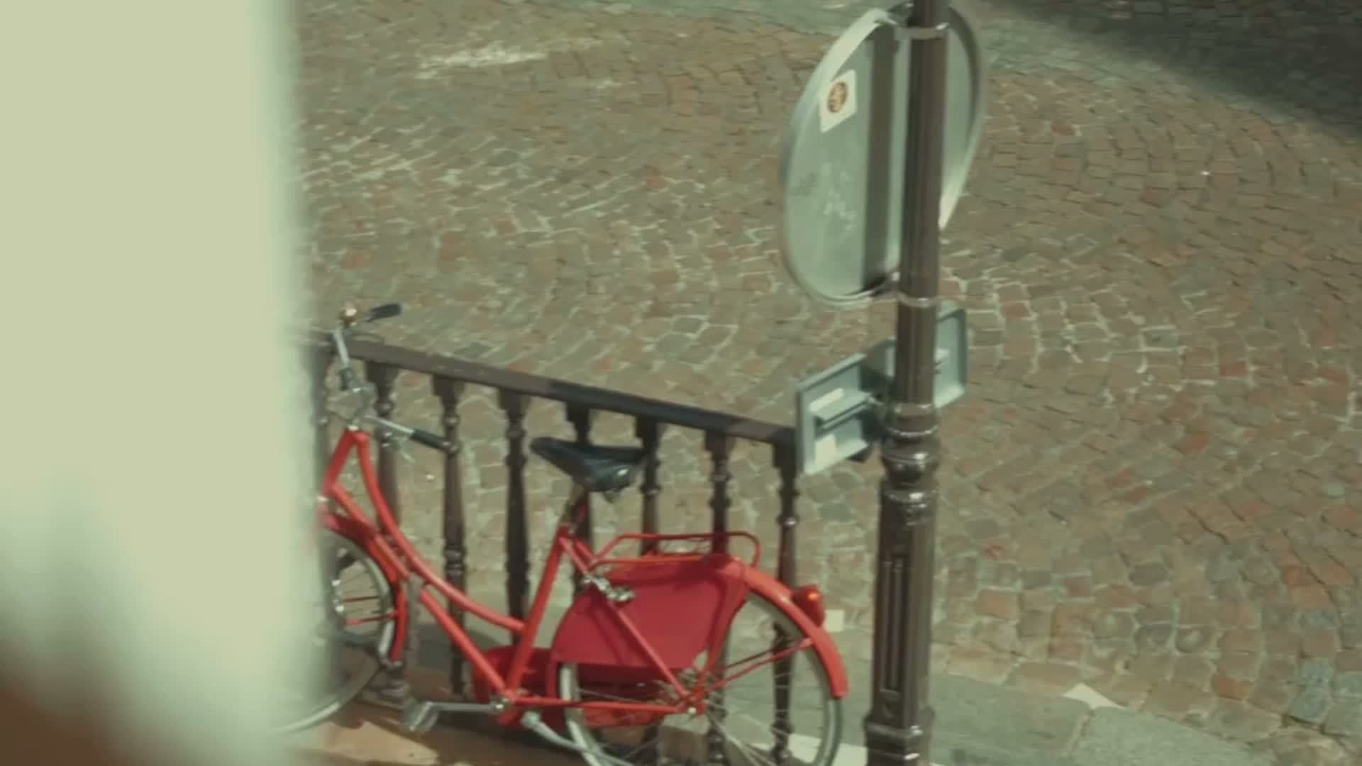 Vélo rouge garé à côté d'une barrière en métal sur un trottoir pavé.