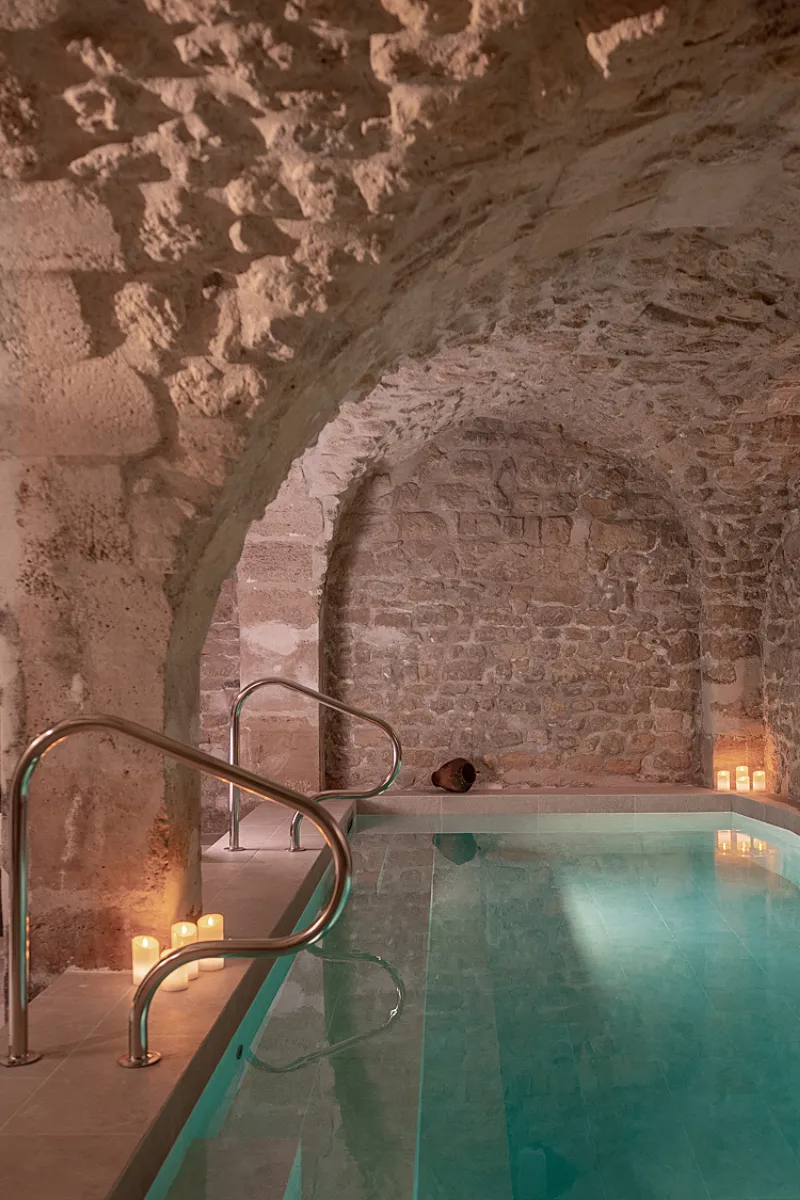 Piscine intérieure dans une salle voûtée en pierre avec bougies allumées sur les côtés.