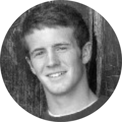 Black and white portrait of a young man smiling in front of a wooden background.