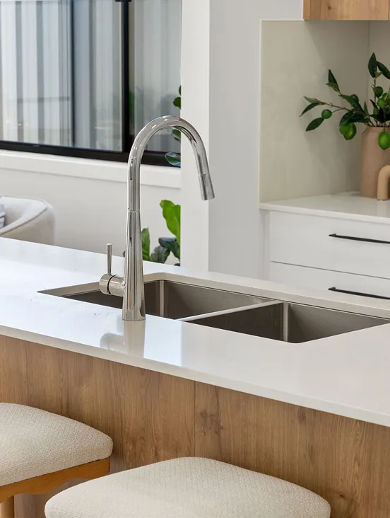 Modern kitchen in a PlanCo Homes custom build, featuring a tall curved stainless steel tap, white stone countertop, timber panelling and beige cushioned stools