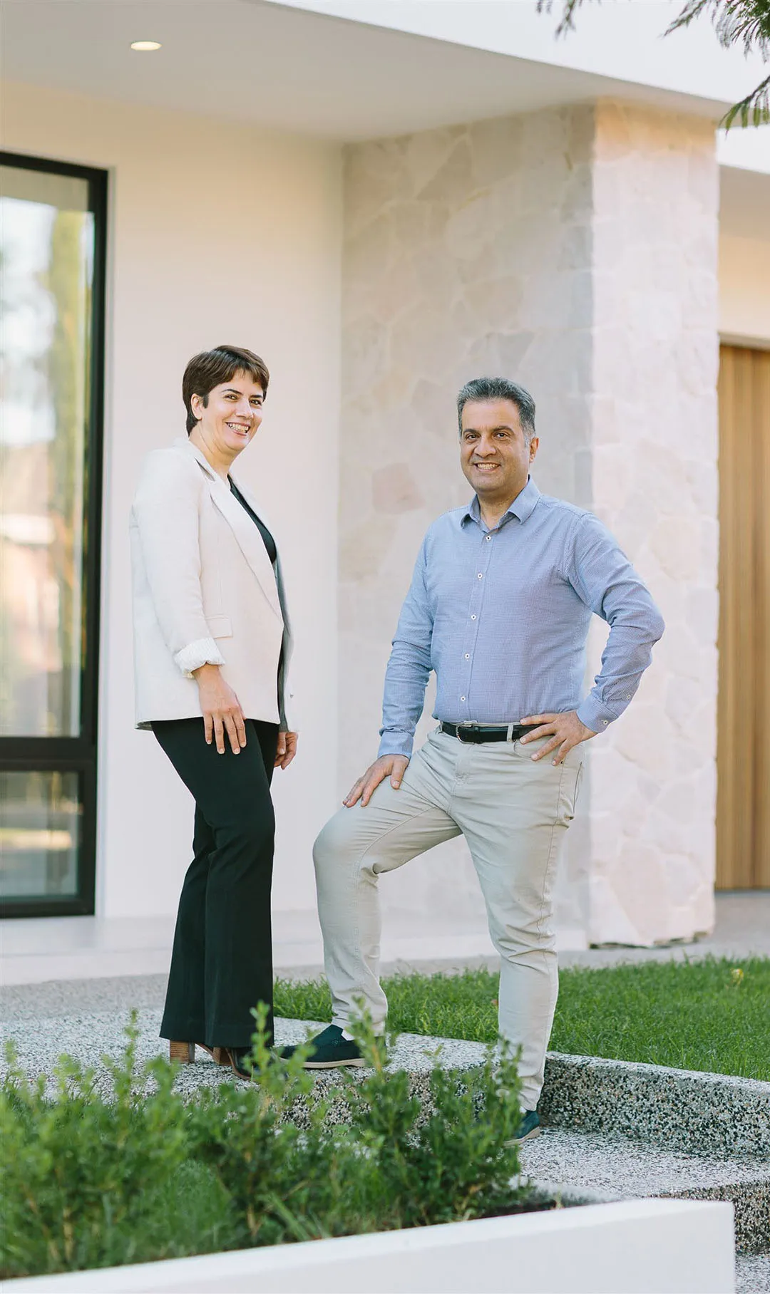 Smiling man and woman standing outside a modern building with greenery in front.