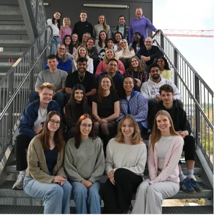 Group of diverse young adults and adults sitting on outdoor stairs smiling at the camera.