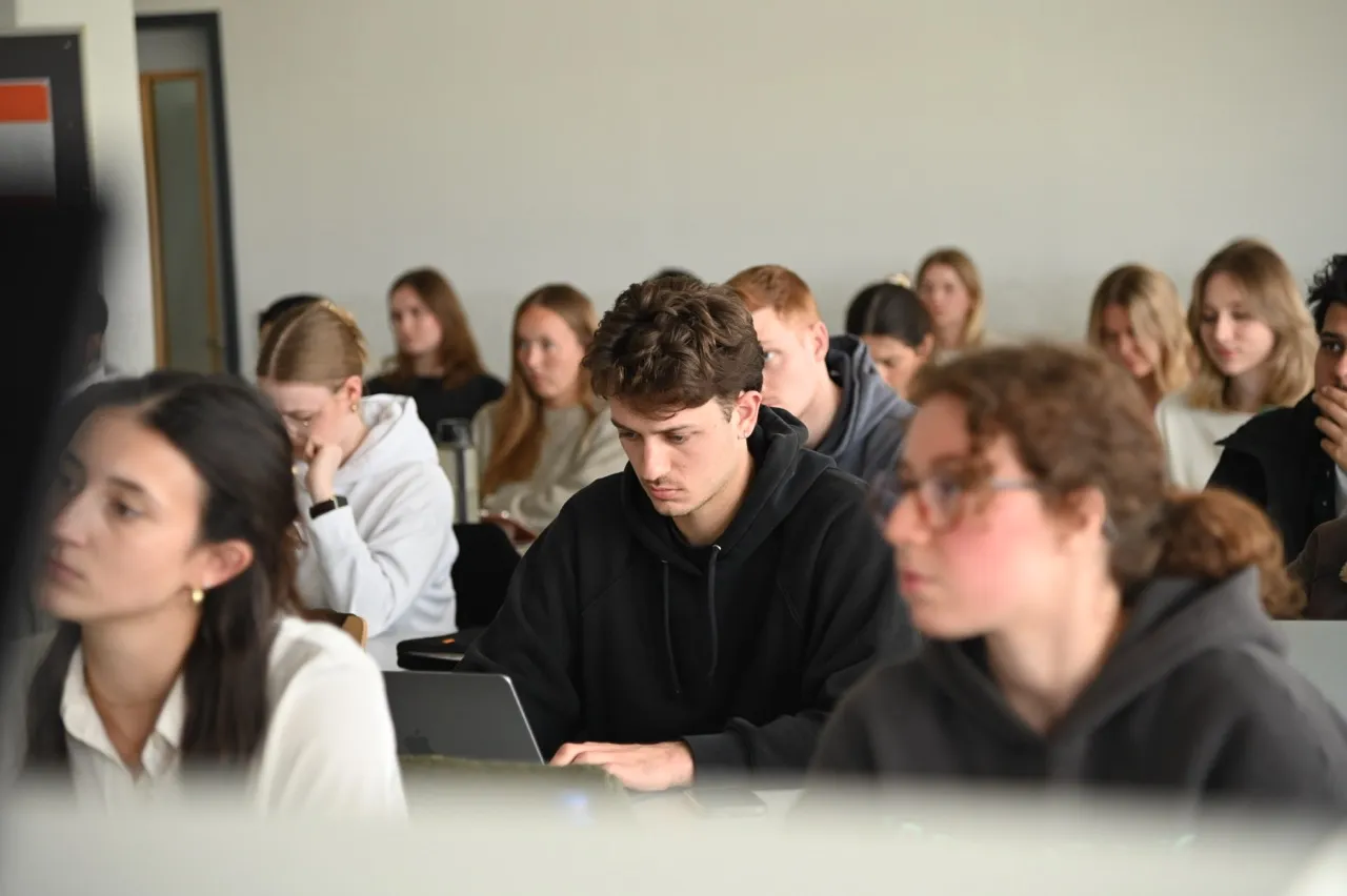 Students in a classroom focused on laptops and notes, engaged in studying or lecture.