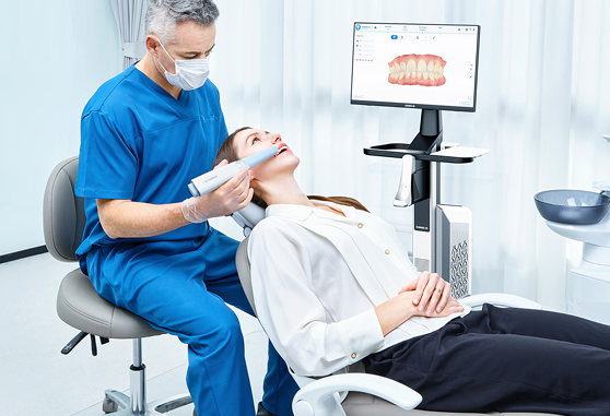 Dentist in blue scrubs scanning a patient's teeth with a digital intraoral scanner.