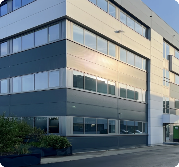 Modern office building with large windows reflecting sunlight and green plants outside.