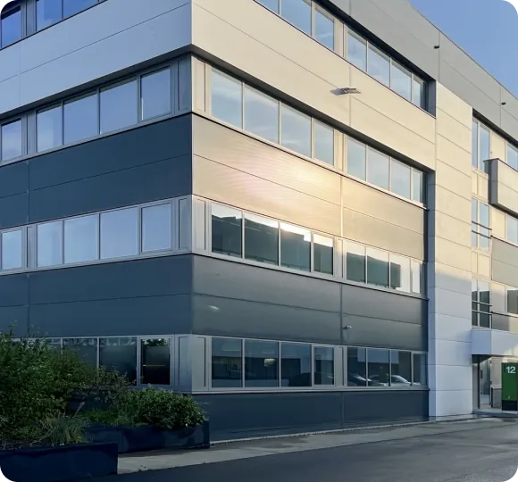 Modern office building with large windows reflecting sunlight and green plants outside.
