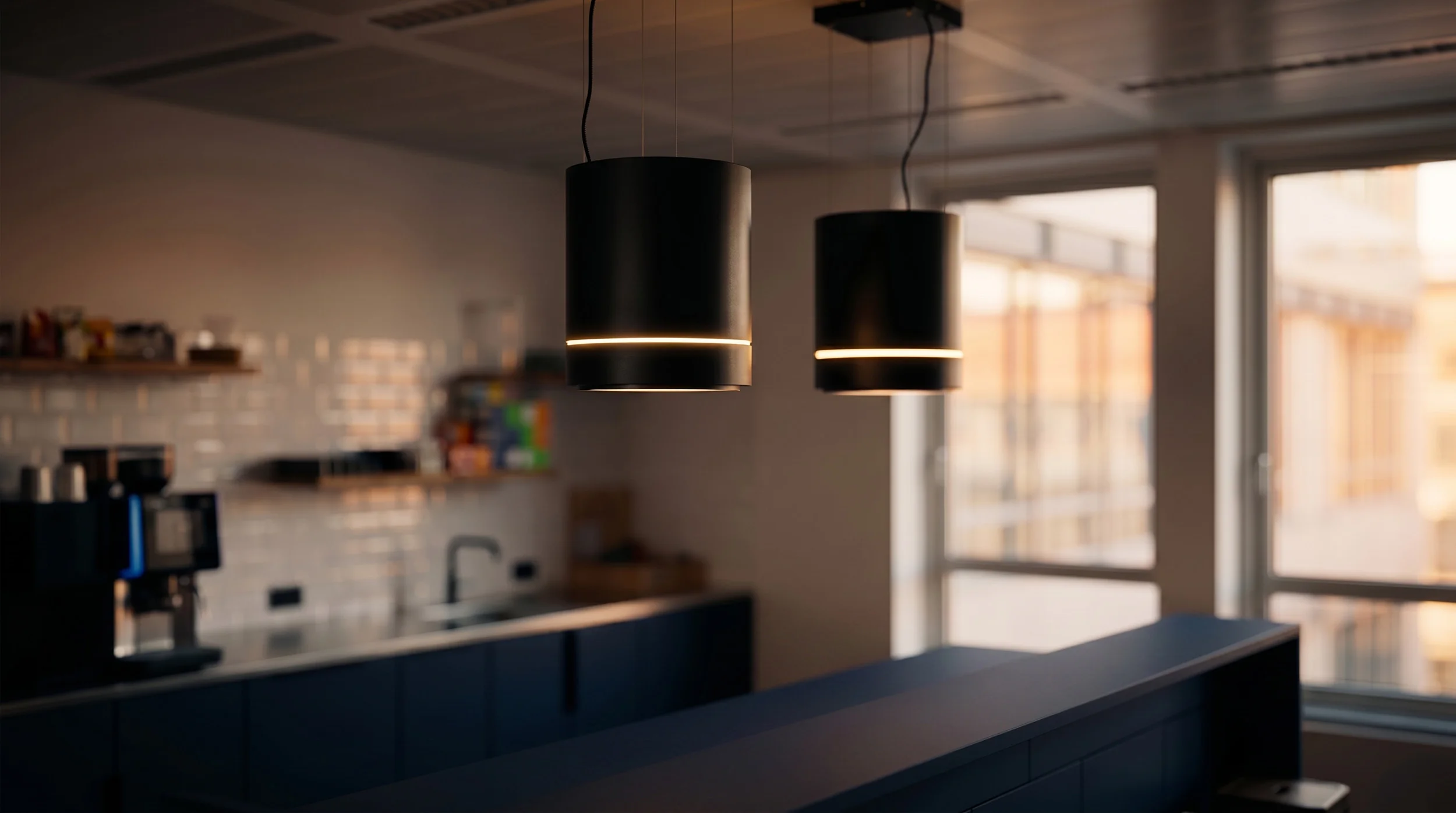 Zwei schwarze Pendelleuchten über einer Office-Küche mit Theke im Hintergrund.