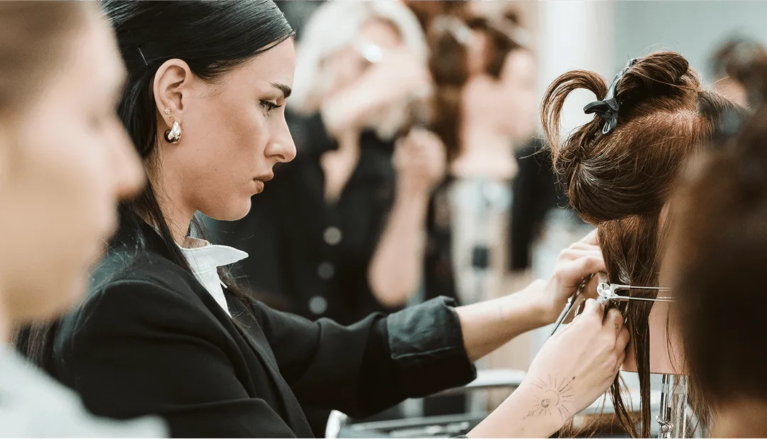 Stylistin schneidet Haare in einem Salon, konzentriert arbeitend, umgeben von anderen Friseuren, Fokus auf Präzision.