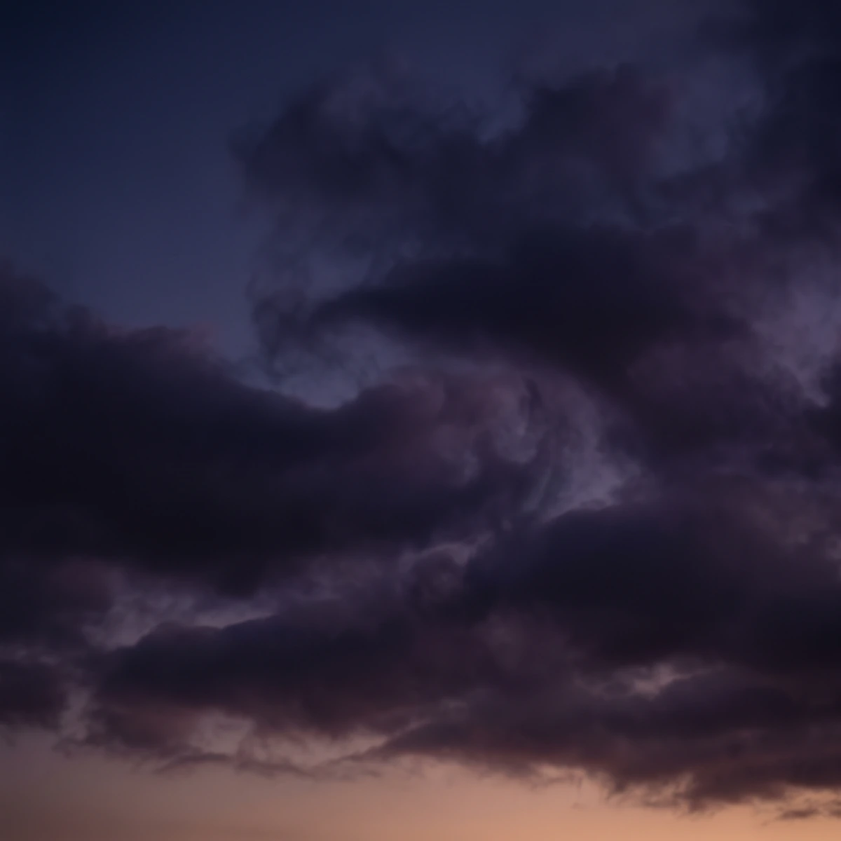 Soft clouds drifting at dusk in deep indigo and plum with a faint warm glow along the horizon.