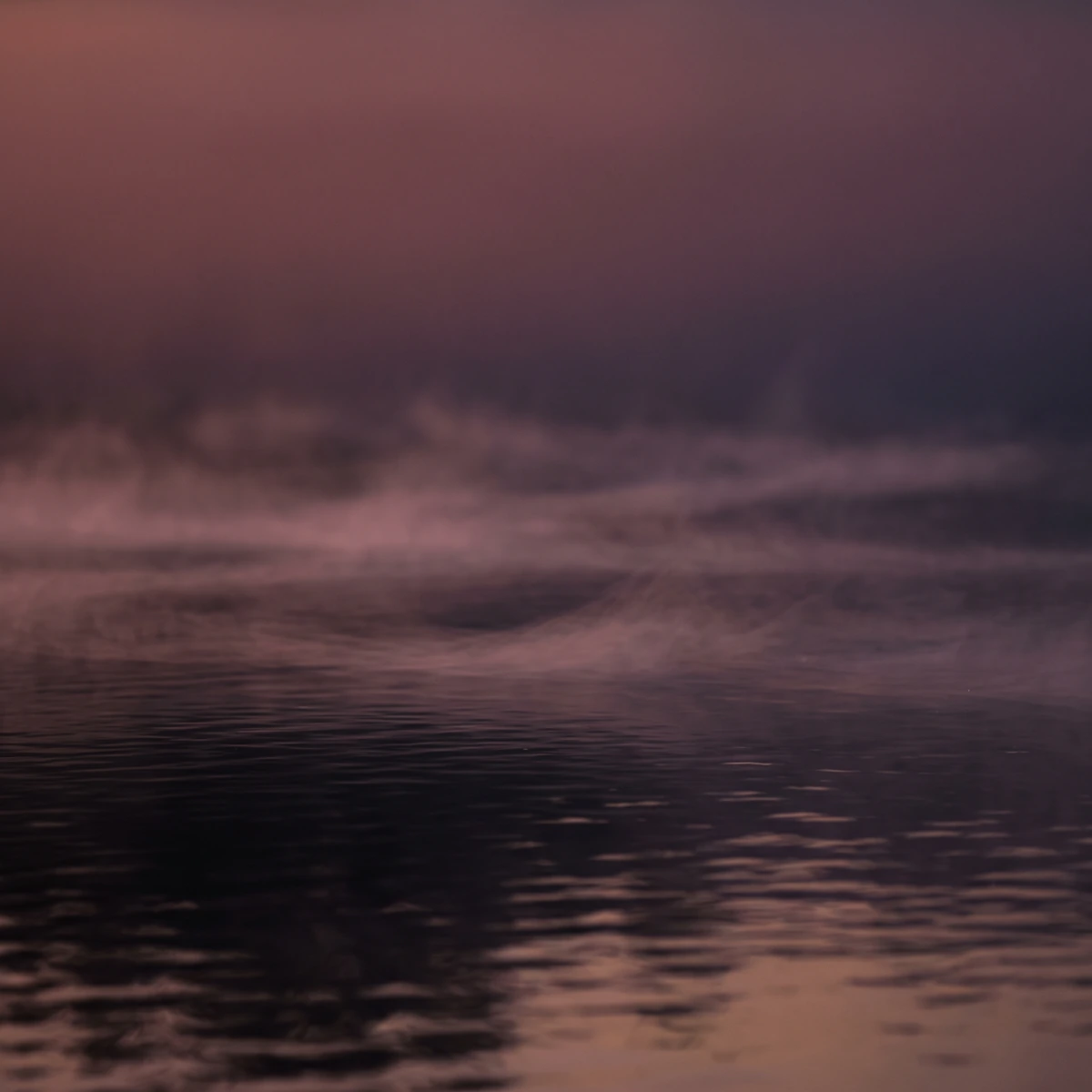Soft mist drifting over dark still water at dusk in muted rose and plum tones.
