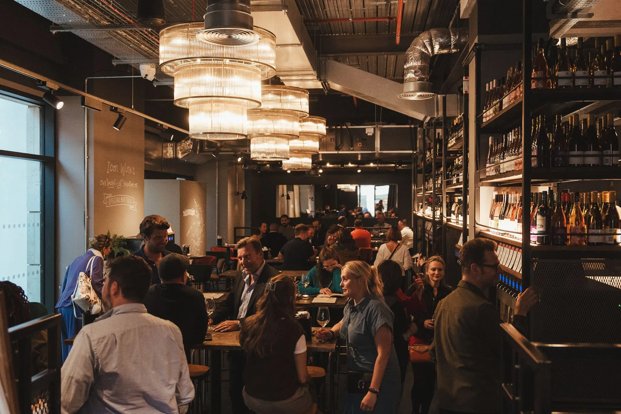 A busy evening at Vagabond St Pauls, with guests beneath large chandeliers and walls of wine