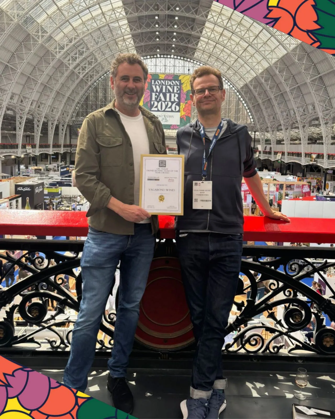 Two men on a balcony at the London Wine Fair 2026 holding a Vagabond Wines award certificate