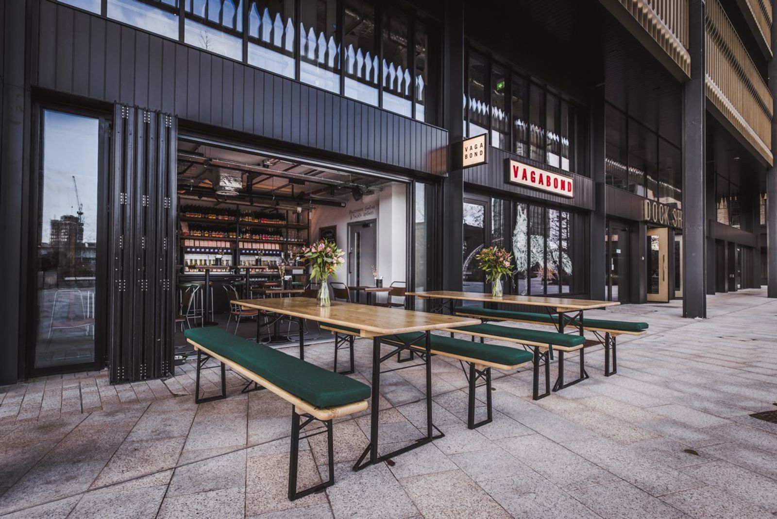 Green picnic benches outside the entrance to Vagabond Canada Water