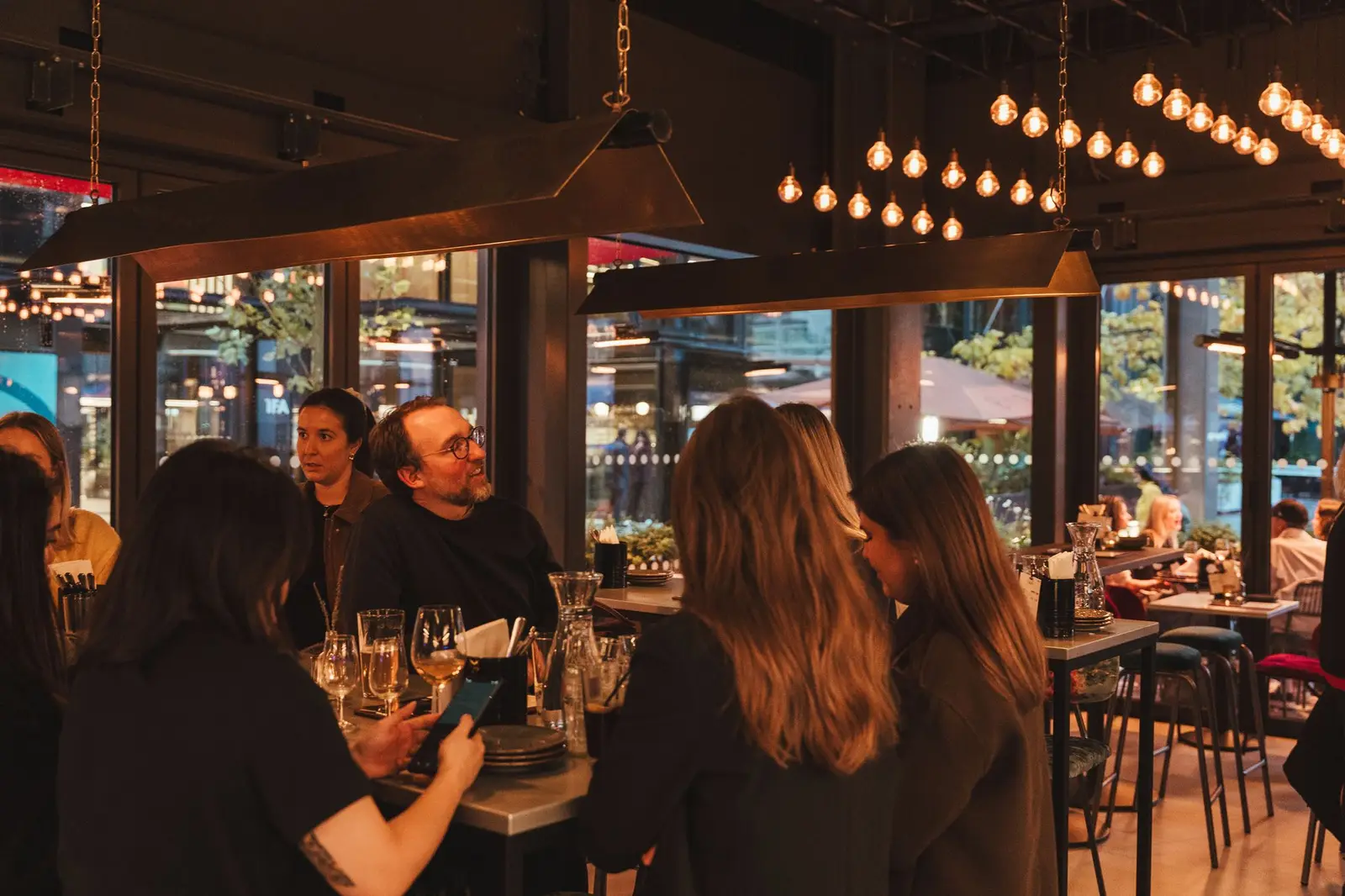 Friends sharing wine at a table by the windows of a Vagabond wine bar in the evening