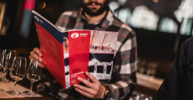 Student reading a WSET Level 1 course book beside tasting glasses at the Vagabond Wine Academy