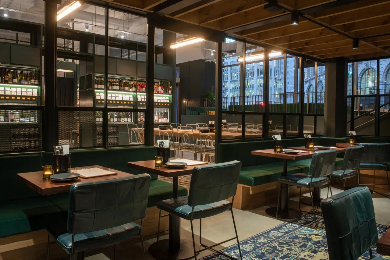 Green leather booths and wooden tables in a glass-walled dining area at Vagabond Monument