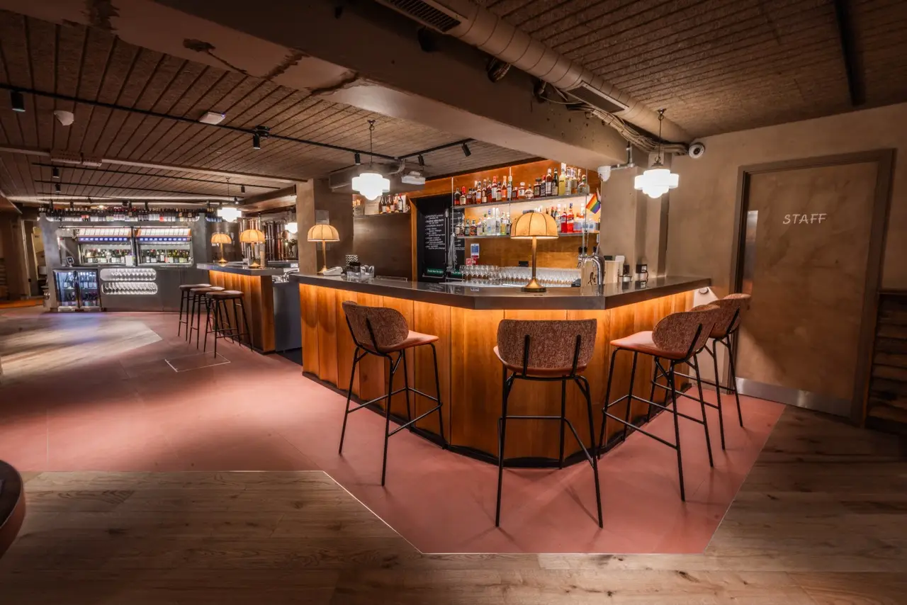 Curved wooden bar with high stools and warm pendant lights at Vagabond Carnaby