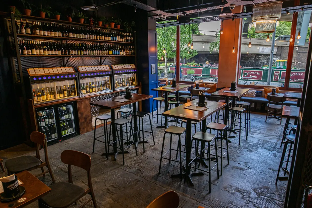 High tables and self-pour wine machines at Vagabond Paddington, with narrowboats visible through the windows