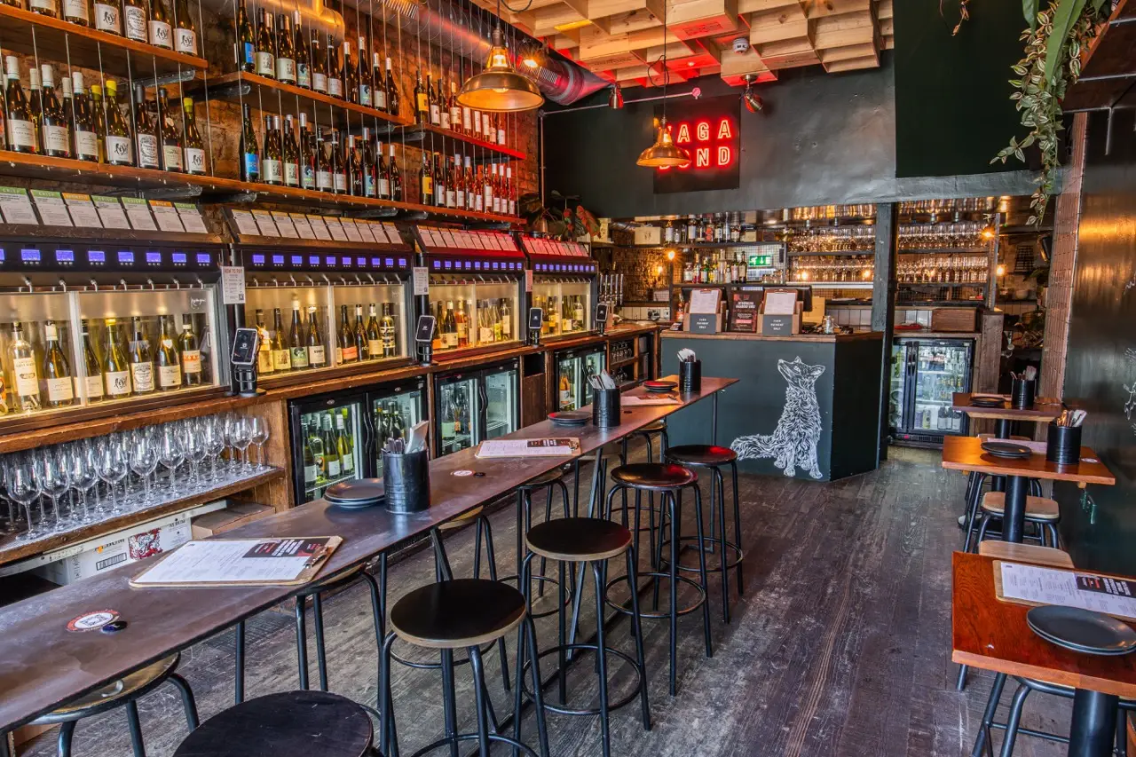 Self-pour wine machines along the bar under a red neon Vagabond sign at Vagabond Northcote Road