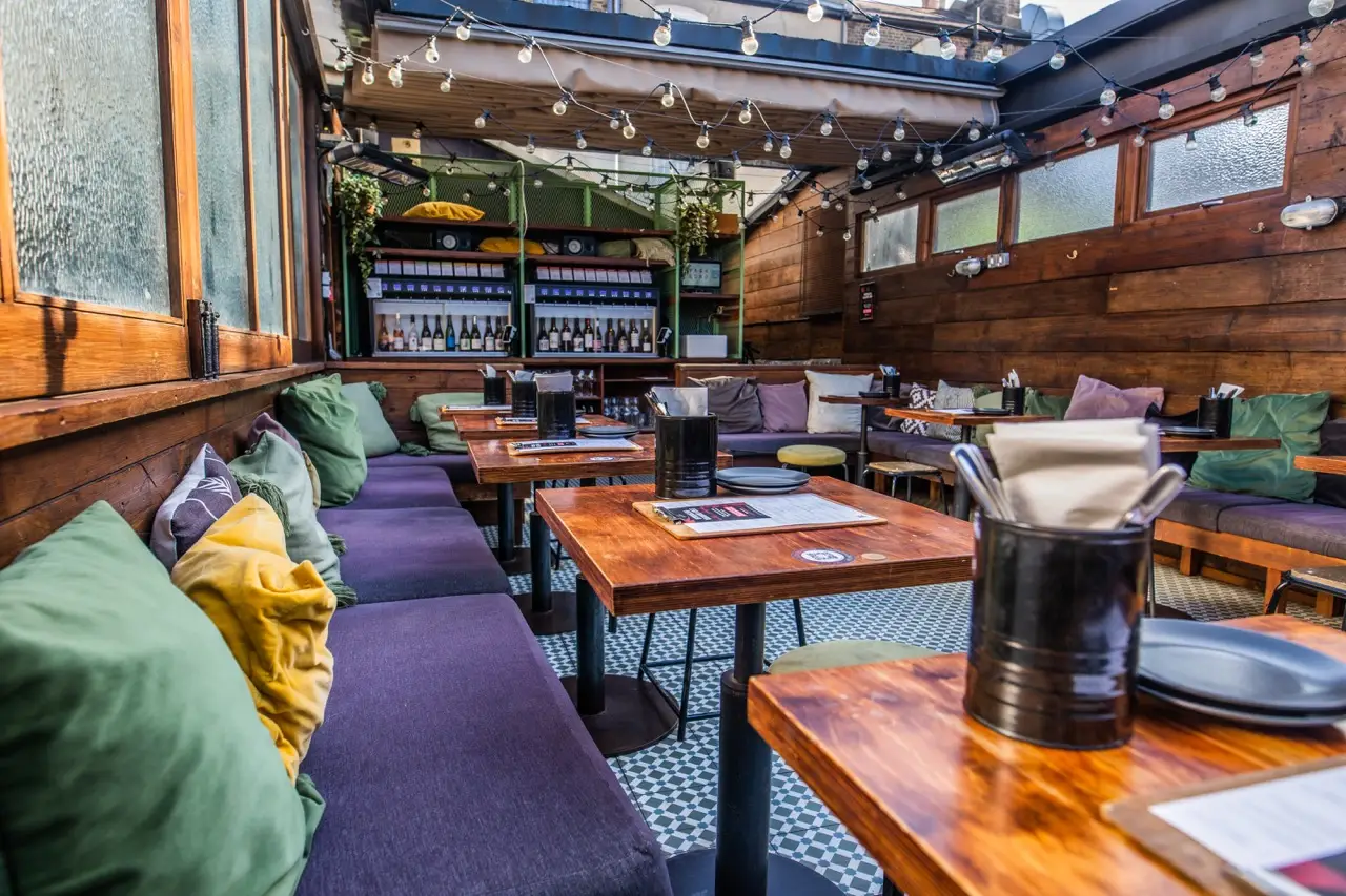 Covered roof terrace with purple banquettes, cushions and festoon lights at Vagabond Northcote Road