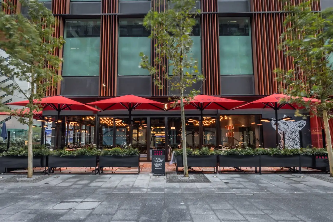 Glass frontage and terrace with red parasols at Vagabond Liverpool Street in Broadgate