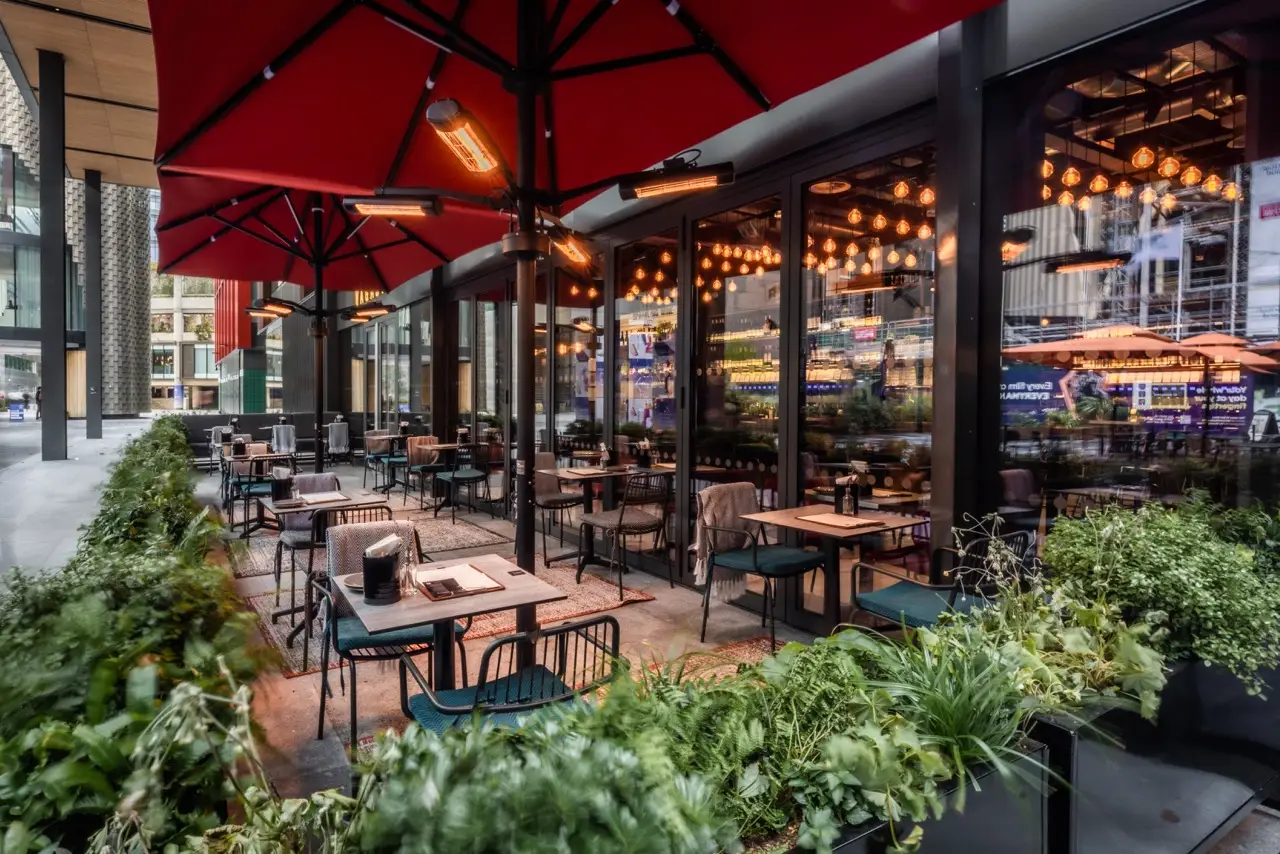 Outdoor terrace with red parasols and planters at Vagabond Liverpool Street, Broadgate
