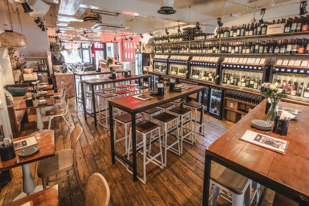 Rows of self-pour wine machines along the wall at Vagabond Charlotte Street, with wooden high tables and stools