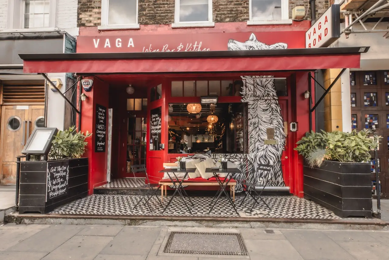 Red shopfront of Vagabond Wine Bar & Kitchen on Charlotte Street, Fitzrovia, with a tiled entrance and planters