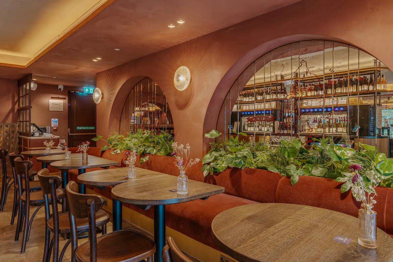 Arched wine displays above planters and café tables at Vagabond Canary Wharf